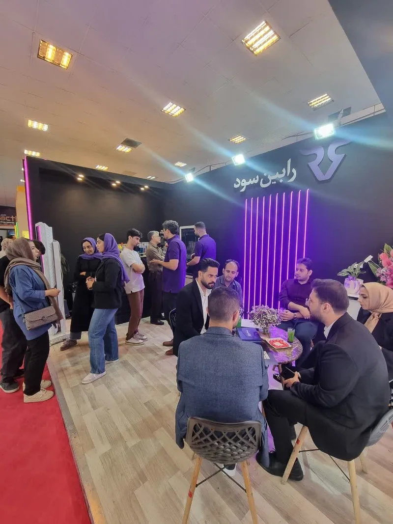 غرفه شلوغ رابینسود با نورپردازی بنفش و بازدیدکنندگان نشسته در نمایشگاه تراکنش ایران